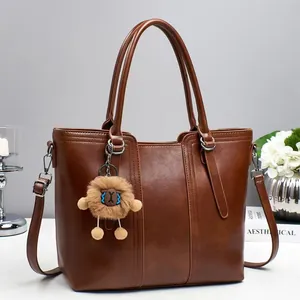 Brown faux leather bucket tote bag with plush charm and adjustable shoulder strap