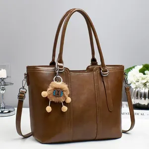 Dark brown leather bucket bag with top handles and plush pendant on a minimal desk