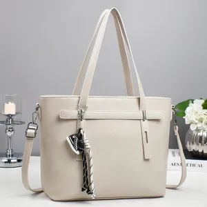 Chic cream leather tote bag with woven tassel and adjustable strap on a modern desk