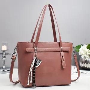 Pink PU leather tote bag with woven tassel charm and adjustable shoulder strap on desk