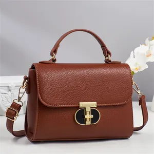 Sac à main marron en cuir avec fermoir doré en T sur un socle en pierre blanche