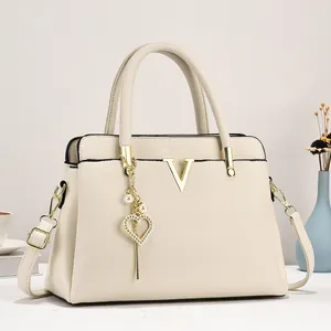 Sac fourre-tout crème chic avec logo V doré et breloque cœur dans un intérieur élégant