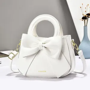 Sac à main blanc en simili cuir avec grand nœud et détails dorés sur fond bleu clair