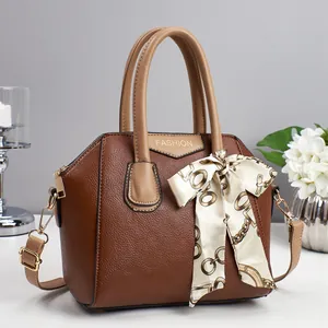 Detail einer braunen Handtasche mit Lederstruktur, Seidenschal und goldener Hardware