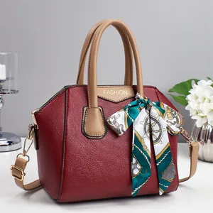 Detail der roten Handtasche aus Narbenleder mit Goldschrift und dekorativem Seidentuch