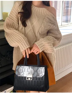 Dettaglio borsa nera con patta a serpente e chiusura dorata abbinata a un maglione beige
