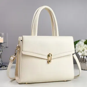 Close-up of minimalist off-white pebble leather handbag featuring a refined golden twist lock