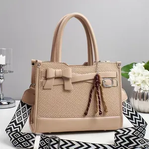 Dettaglio borsa beige con trama intrecciata, fiocco e tracolla geometrica larga