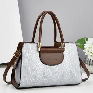Detail of grey snakeskin textured handbag with brown leather trim and gold fashion hardware