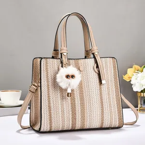 Minimalist straw woven tote bag with brown leather straps and plush charm for summer commute