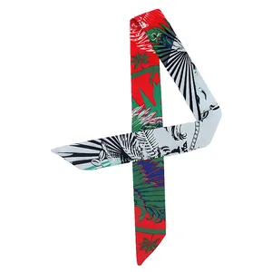 Detalle de un pañuelo twilly sedoso con estampados tropicales de hojas de palma y plumas