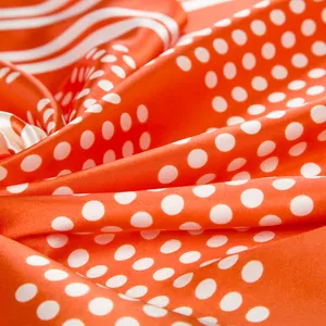 Close-up of orange silk scarf showing white polka dots and stripe pattern texture