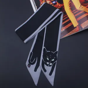 Détail d'un foulard étroit en soie avec imprimé chat noir et yeux verts sur tissu sombre