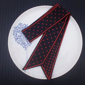 Elegant black twilly scarf with red polka dots on a white decorative ceramic plate