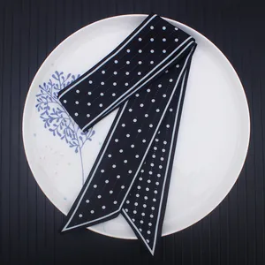 Elegant black twilly silk scarf with white polka dots and bias ends on a ceramic plate