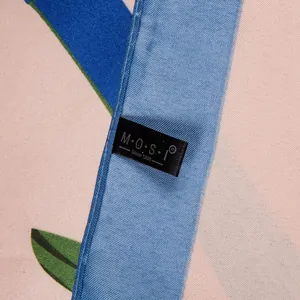 Detail van zijden sjaal met bloemenprint en ingenaaid M·O·S·I merk geweven label