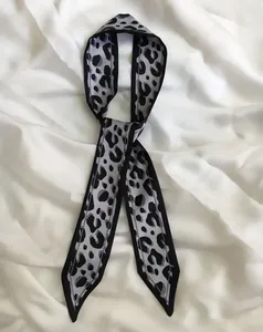 Classic grey and black leopard print skinny scarf tied elegantly on a soft white silk background