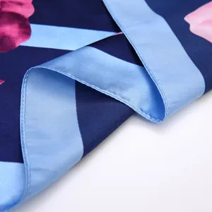 Detail of silk scarf showing deep blue floral print with hand-rolled edges and satin texture