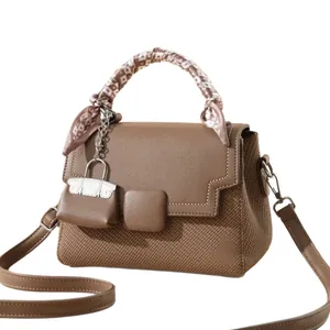 Brown rectangular crossbody bag with scarf-wrapped handle and mini charm on white background
