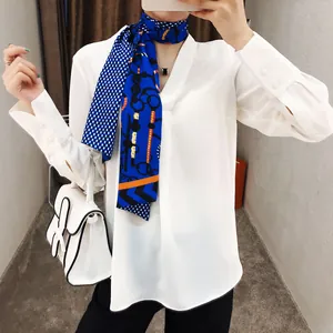 Detail van zijden sjaal met ketting- en riemprint op een witte chiffon overhemdblouse