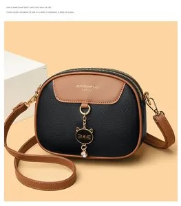 Detail of crossbody bag featuring dual zippers, cat charm and litchi grain leather texture