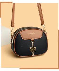Detail of dual zipper compartments and rhinestone cat charm on leather crossbody bag