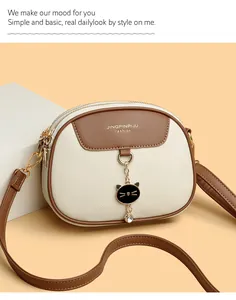 Detail of cream round crossbody bag with brown trim and cute black cat metal pendant