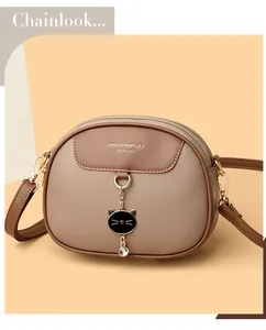 Close-up of beige and brown crossbody bag with rhinestone kitten charm and gold zippers
