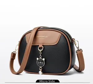 Detail view of round crossbody bag with leather texture and cat pendant decoration