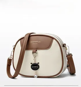 Detail of cream crossbody bag with leather texture, dual zippers, and cat charm