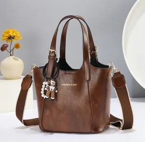 Brown vintage leather bucket bag with top handles, wide strap and doll charm detail