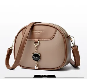 Detailed view of khaki oval crossbody bag with cat charm and double zipper closure