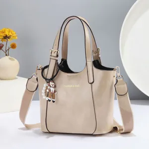 Detail of beige faux leather tote featuring gold lettering and cute doll charm with pearls