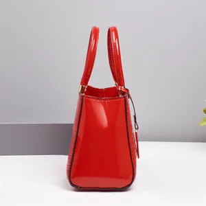 Detail view of red glossy patent leather handbag with embossed crocodile texture and gold hardware