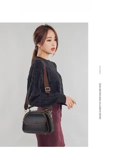 Detail of a vintage black lychee leather crossbody bag with brown trim and metal logo plate