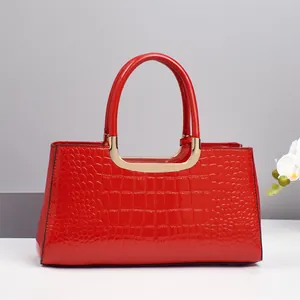 Detailed view of red crocodile-patterned patent leather bag with gold metal handle base