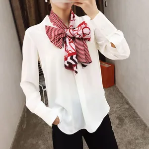 Detail van een witte chiffon blouse met een grote rood-roze satijnen sjaal met patronen
