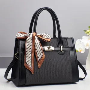 Chic black quilted handbag with silk scarf handle and golden hardware on a white table