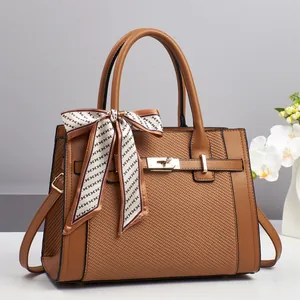 Detail of a brown shoulder bag featuring woven texture and a decorative silk handle scarf