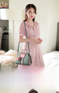 Detail of color-block handbag with pink plush ball charm and striped ribbon strap
