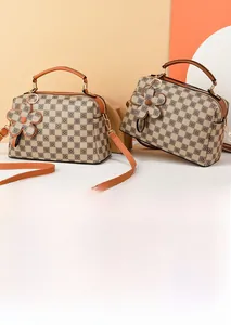 Detail view of brown checkered satchel with floral charm and adjustable shoulder strap