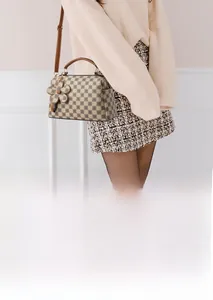 Classic checkered pattern handbag detail with floral charm and adjustable strap