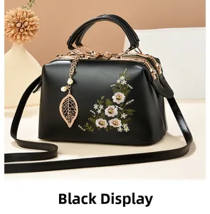 Close-up of black handbag featuring intricate floral embroidery and gold leaf pendant