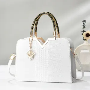 White crocodile pattern handbag with woven handle and elegant pearl charm on minimalist background