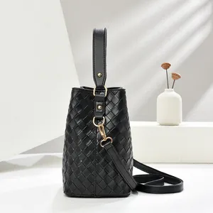 Sac seau tissé noir avec ferrures dorées et bandoulière réglable sur socle minimaliste
