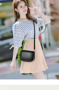 Minimalist black matte leather saddle bag with flap detail shown on a model outdoors