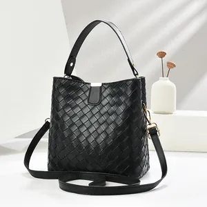 Sac seau tressé noir avec poignée supérieure et boucles dorées sur support blanc épuré