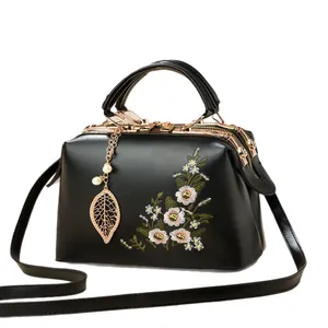 Elegant black handbag with floral embroidery, gold leaf pendant, and top handle detail