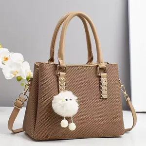 Brown woven texture handbag with leather handles and a white plush ball charm