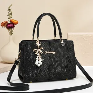 Elegant black snake pattern tote bag with gold logo and pearl bow charm on beige background